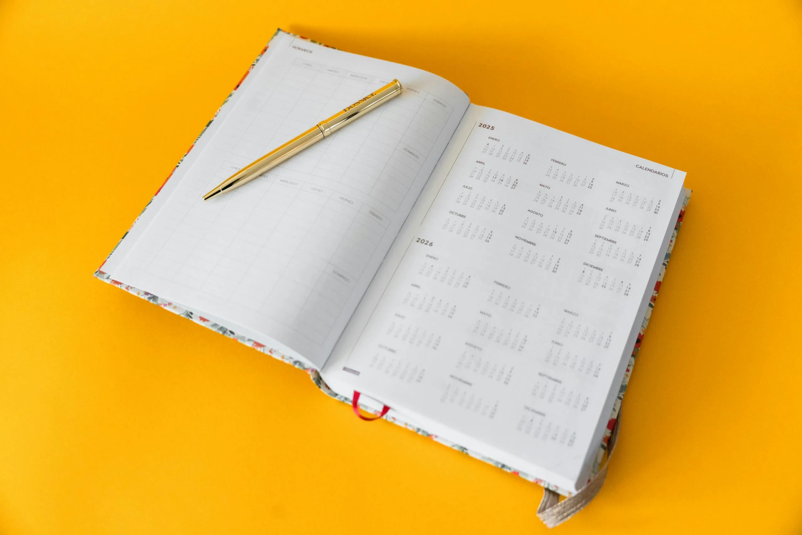 Open planner for 2023-2025 with a golden pen on a vibrant yellow background, perfect for organizing and planning.